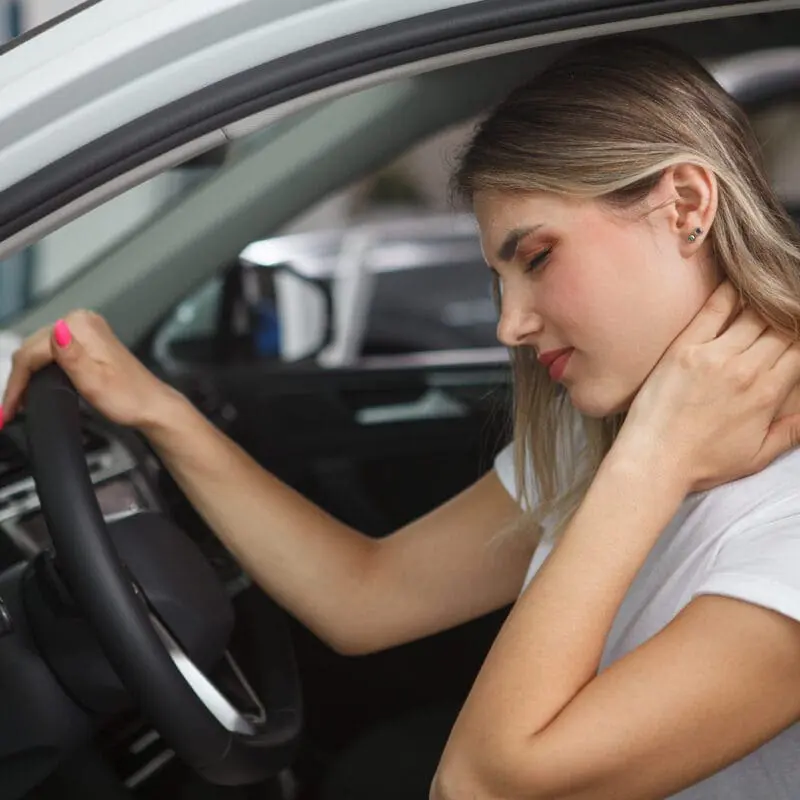 a woman holding her neck and looking at the wheel of a car. Common Injuries from Car Accidents