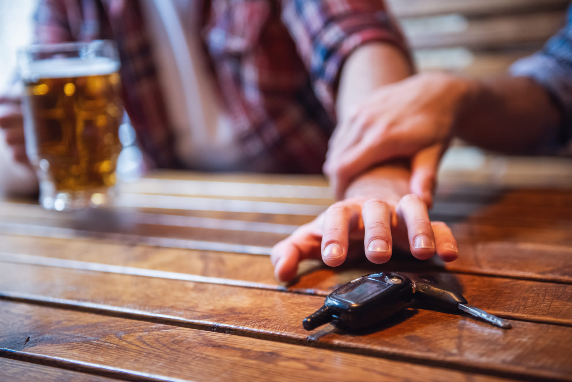 man stopping his friend from driving drunk by keeping his car keys away at the bar