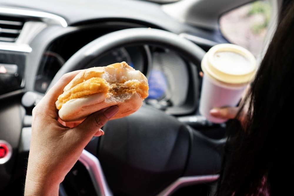distracted driver holding coffee and eating a breakfast sandwich while driving