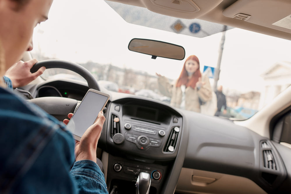 distracted driver looking at phone while pedestrian steps into road